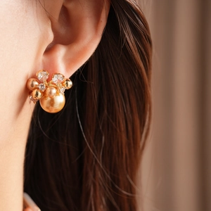 Detail view of pearl and zircon flower earrings on model with warm golden tones
