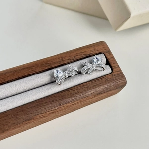 Macro shot of silver bow stud earrings with heart-shaped zircon in a wooden jewelry box