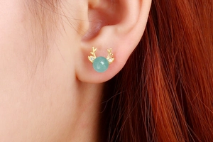 Detail of golden reindeer antler earrings with green gemstone on a female model