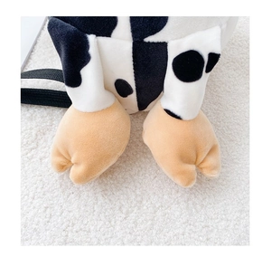 Detail of soft plush cow bag with black and white spots and brown feet on white fabric