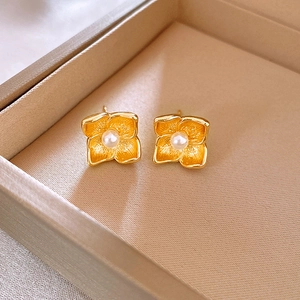 Elegant gold flower stud earrings with white pearl center on luxury jewelry box