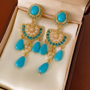 Vintage gold earrings with turquoise stones and pearls on a champagne velvet background