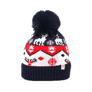 Close-up of reindeer and snowflake jacquard knit patterns on winter hat with fluffy pompom
