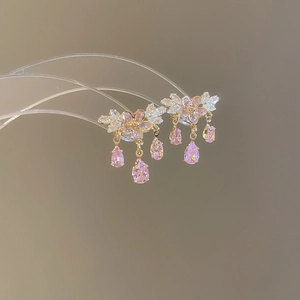 Dettaglio di orecchini a fiore rosa con nappe di zirconi e finitura oro