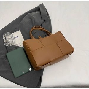 Flat lay of brown woven leather tote bag with lifestyle accessories on white fabric