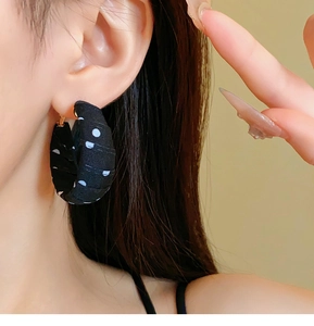Close-up of retro C-shaped earrings featuring black fabric with white polka dots pattern