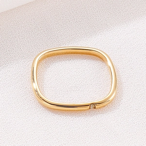 Macro shot of minimalist gold square ring with single diamond on white fabric texture