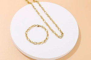 Detail view of gold stainless steel necklace and bracelet set on a white round pedestal