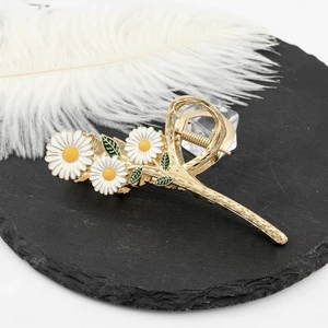 Detail of gold metal hair claw clip featuring white daisy flowers and green leaf accents