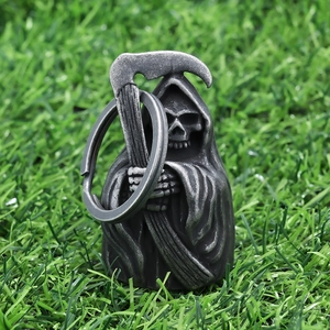 Detailed close-up of a vintage grim reaper skull bell pendant on green grass background