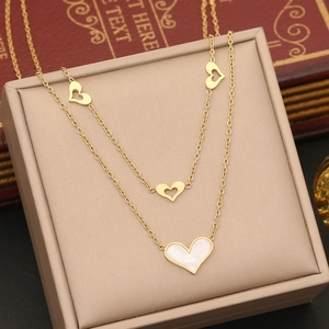 Close-up of golden double-layered heart necklace with white shell inlay in a beige jewelry box
