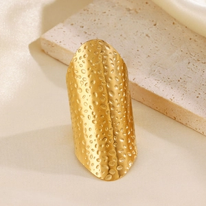 Golden stainless steel hammer texture wide shield ring standing on beige stone
