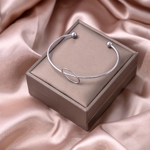 Close-up of a silver metal open bangle with round charm on a luxury satin background