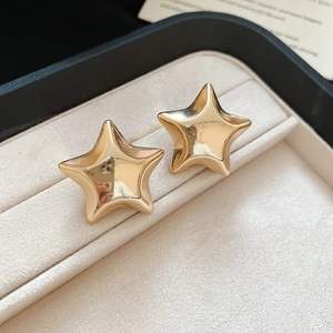 Macro view of gold star stud earrings with a glossy metallic finish on a velvet base