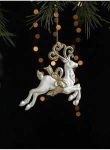 Détail d'un ornement de Noël renne blanc perle avec paillettes dorées sur une branche de sapin