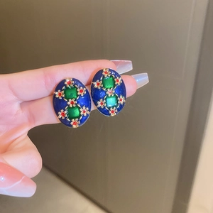 Close-up of vintage blue enamel earrings with green gems and golden flower details