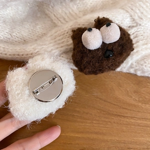 Close-up of plush cartoon bear brooch with white pom-pom on knitted sweater