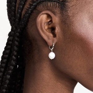 Close-up of a silver hoop earring with a baroque white pearl on a woman's ear