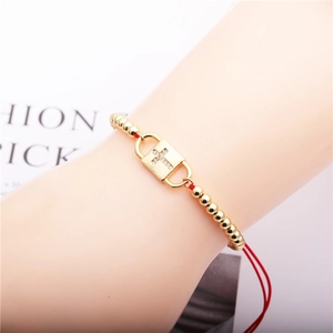 Detail of red cord bracelet with gold beads and zircon-encrusted cross lock pendant