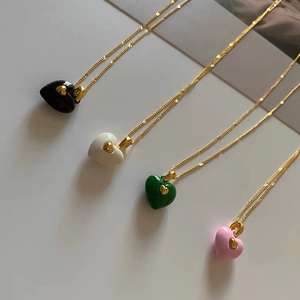 Detail view of four colorful enamel heart necklaces in black, white, green, and pink colors