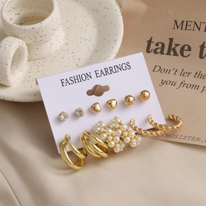 Detail of a 6-piece gold earring set with pearls and zircons on a textured cream backdrop
