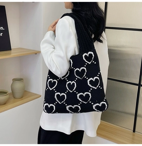Sac à épaule en tricot noir avec motif de cœur blanc porté par un mannequin
