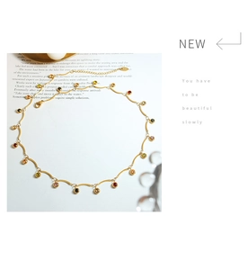 Détail de la chaîne à vagues plaquée or 18K avec zircons multicolores sur surface blanche
