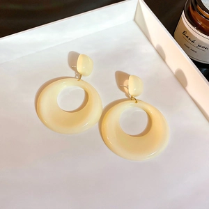 Détail de boucles d'oreilles créoles en acrylique crème avec maillons dorés sur plateau