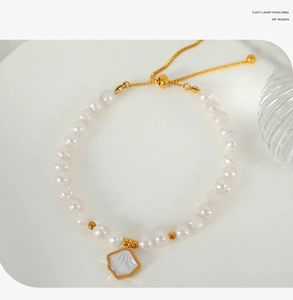 Detail of freshwater pearl bracelet with gold beads and shell pendant on white plate