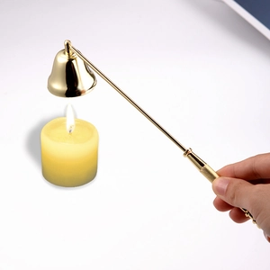 Golden metal candle snuffer with long handle extinguishing a yellow candle on white background