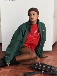 Detail of street style layering with dark green jacket, red hoodie, and leather bag