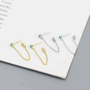 Macro shot of silver and gold tassel chain earrings with turquoise studs on paper