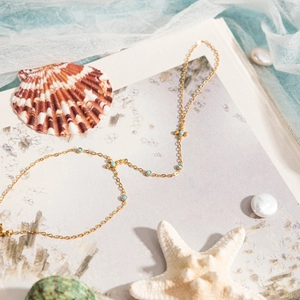 Detail of a gold stainless steel finger bracelet with blue stones and sea shells decor