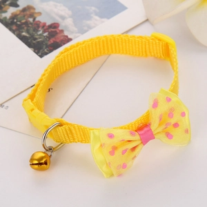 Macro detail of yellow polka dot pet bow tie collar with a golden bell on white surface