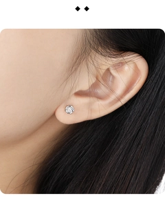 Macro shot of silver rose-shaped stud earring with a clear stone on the earlobe