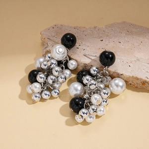 Close-up of pearl and black bead tassel earrings on a textured stone display
