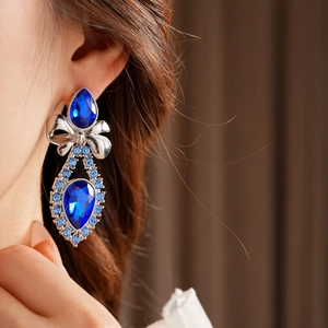 Close-up of blue water drop gemstone earrings with silver bow design and sparkling rhinestones