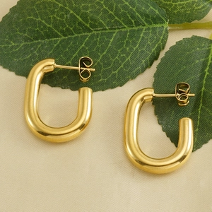 Polished 18k gold U-shaped stainless steel earrings on a soft fabric with green leaves
