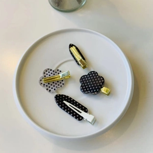 Close-up of four thick acrylic hair clips with black and white polka dots on a plate