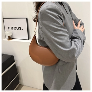 Side view of a brown half-moon PU leather underarm bag worn with a grey blazer