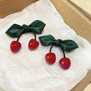 Detailed shot of cherry hair clips with red fruit beads and green satin bows in a gift box