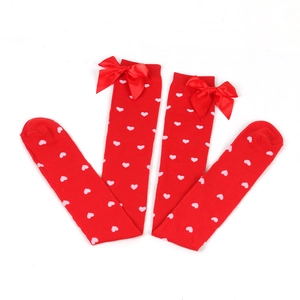Detail of red over-the-knee socks with white heart patterns and festive ribbon bows