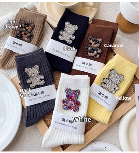Collection of colorful knitted ribbed socks with rhinestone bear patches in a wooden tray