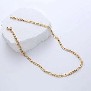 Detailed view of golden Figaro chain necklace with lobster clasp on white stone