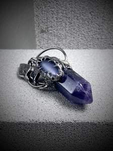 Macro detail of antique silver dragon claw holding a hexagonal amethyst crystal pendant