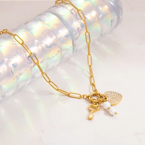 Detailed close-up of golden paperclip chain necklace with heart, key, and pearl charms