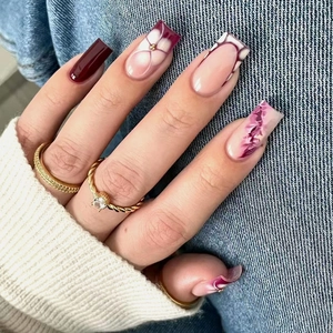 Detail of burgundy and floral press-on nails on hands with a golden gemstone ring