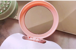 Detail of pink portable folding mirror with adjustable hinge on marble background