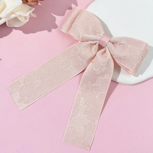 Detailed view of pink jacquard bow hair clip with flowing ribbons on a white tray