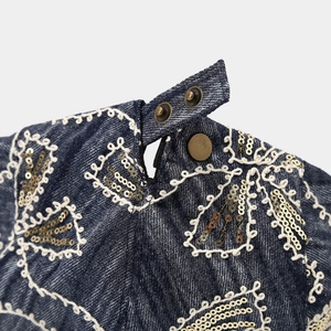 Detailed close-up of blue denim texture with geometric embroidery and gold sequins